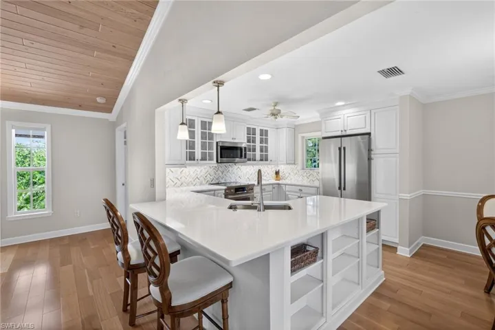 Kitchen featuring a waterfall-edge island with integrated shelving, white shaker cabinetry, stainless steel appliances, and a herringbone tile backsplash