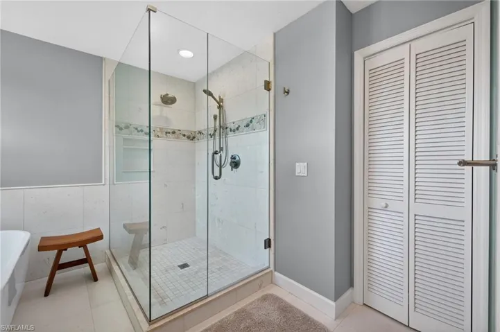 Glass-enclosed shower with white tiled walls, decorative tile accent, and recessed lighting