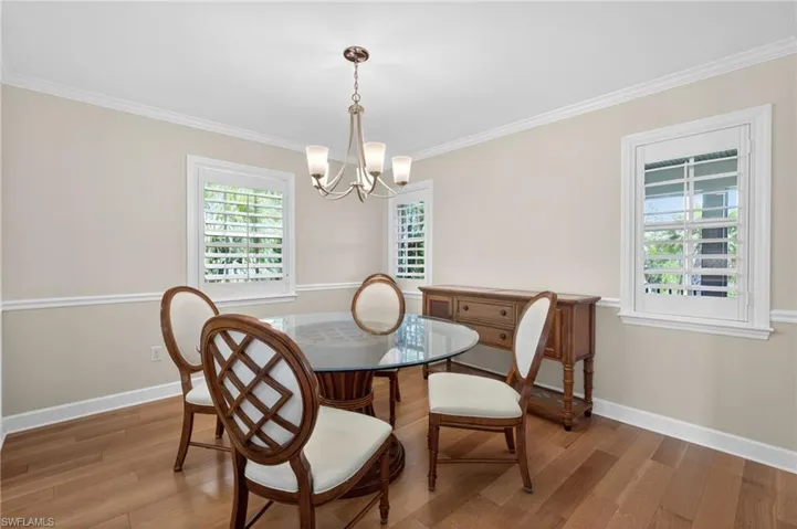 Dining area featuring wood-finish flooring, crown molding, chair rail molding, and two windows with white plantation shutters