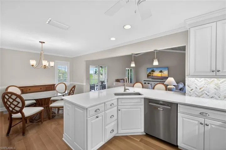 Kitchen featuring white cabinetry, stainless steel appliances, a white countertop island with an undermount sink, and a herringbone tile backsplash