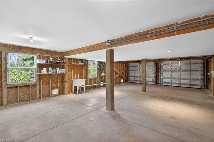 Spacious garage area featuring two overhead garage doors, concrete flooring, exposed wood framing, and multiple windows