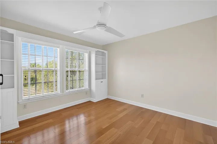 Room featuring two large windows with horizontal blinds, built-in white shelving, wood-finish flooring, and a ceiling fan