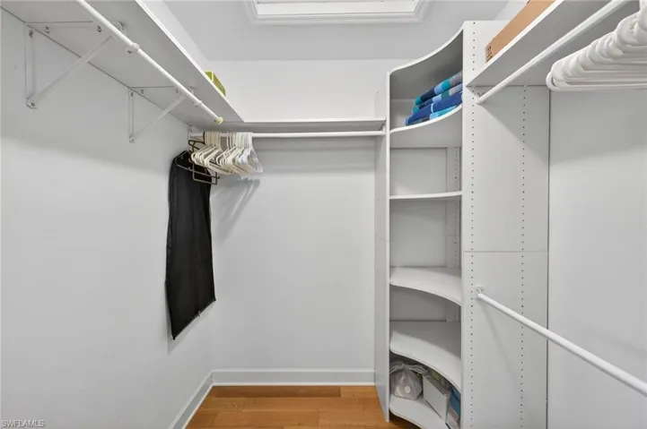 Custom closet organization system featuring white shelving, multiple hanging rods, curved corner shelving, and recessed lighting