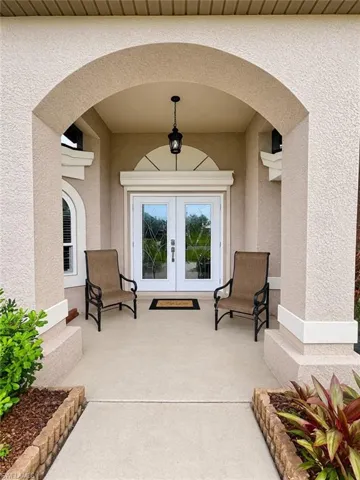 Covered front entry featuring a stucco archway, double doors with decorative glass inserts, a semicircular transom window, and a hanging pendant light