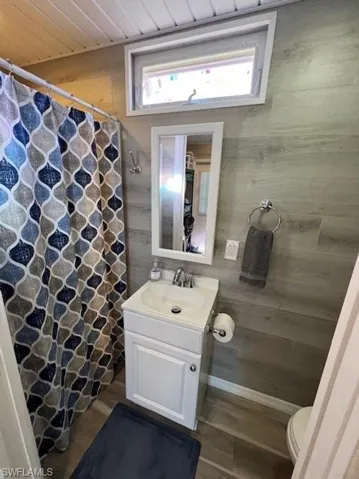 Full bath featuring vanity, wood walls, toilet, plenty of natural light, and wooden ceiling