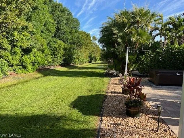 View of green lawn featuring a hot tub and a patio