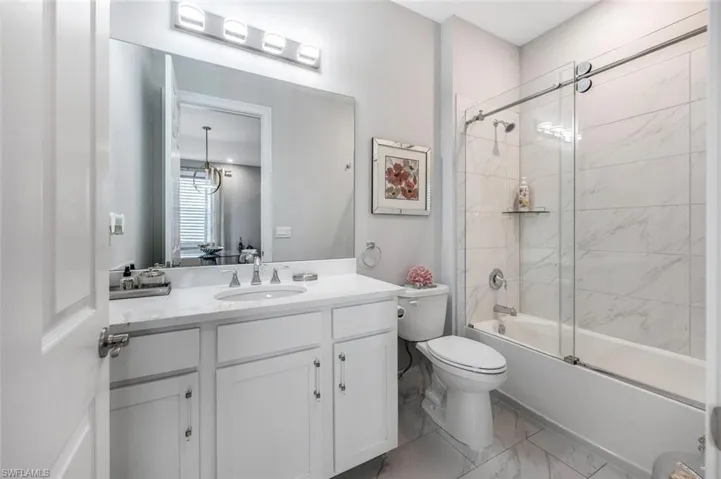 Full bathroom featuring toilet, marble finish floor, bath / shower combo with glass door, and vanity