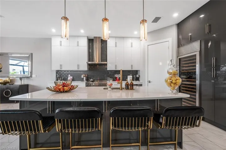 Kitchen featuring a large island, wall chimney exhaust hood, a breakfast bar area, visible vents, and backsplash