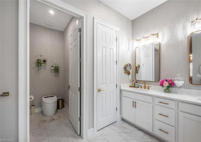 Bathroom with double vanity, marble finish floor, toilet, a sink, and visible vents