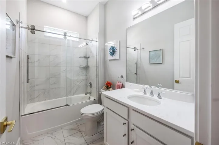 Full bath featuring shower / bath combination with glass door, vanity, toilet, and marble finish floor