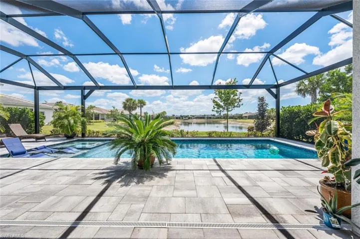 Pool featuring a water view, a patio, glass enclosure, and a hot tub