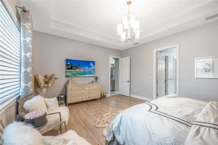 Bedroom featuring visible vents, wood finished floors, a notable chandelier, and a tray ceiling