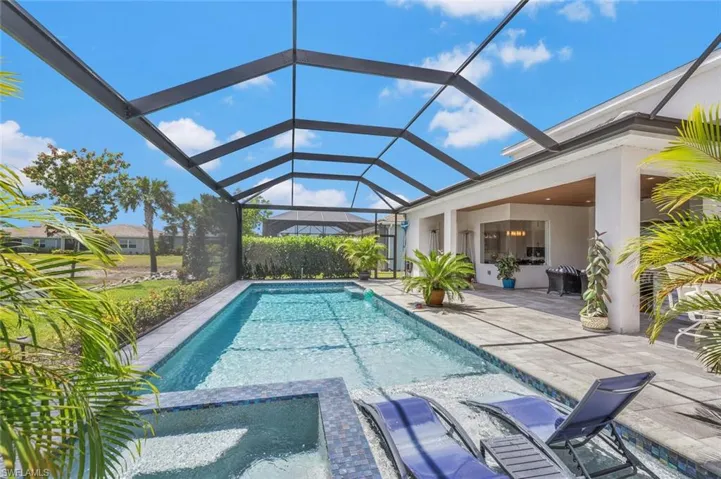 View of pool with a patio, glass enclosure, and a pool with connected hot tub