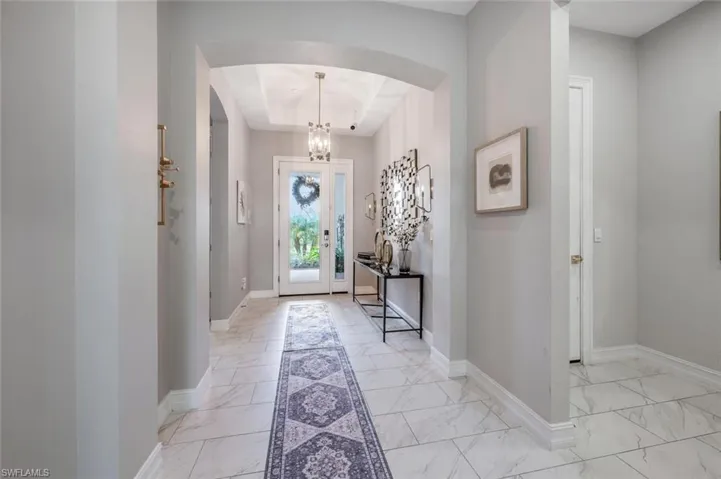 Foyer entrance with arched walkways, marble finish floor, baseboards, a notable chandelier, and a tray ceiling
