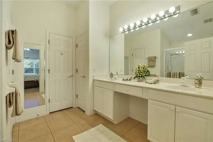 Ensuite bathroom with double vanity, light tile patterned floors, and a stall shower
