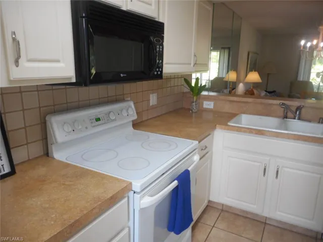 Kitchen with electric range, white cabinetry, black microwave, light tile patterned floors, and open floor plan