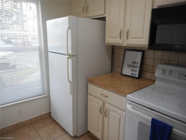 Kitchen featuring white appliances, light tile patterned flooring, light countertops, backsplash, and white cabinetry