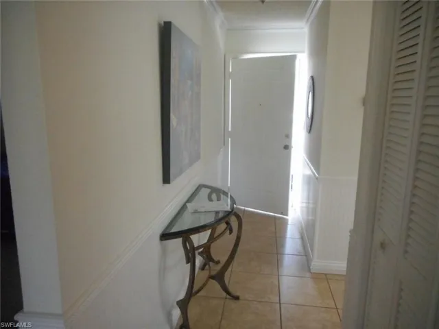 Corridor with wainscoting, light tile patterned floors, and ornamental molding