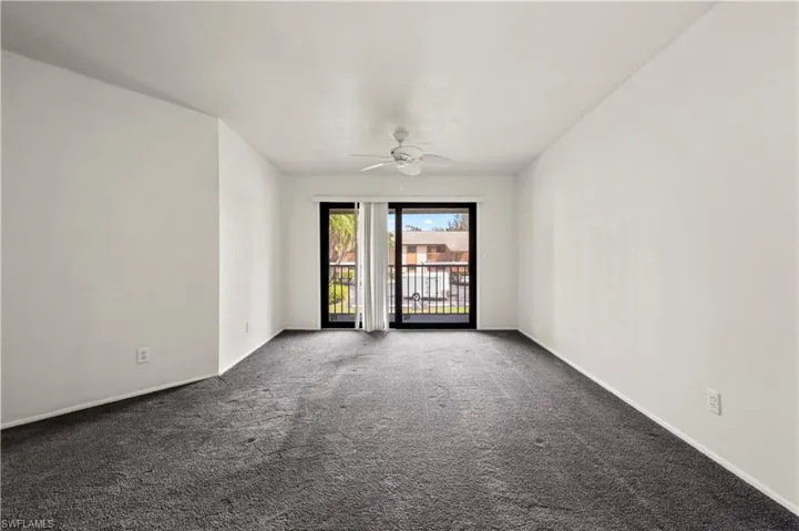 Empty room featuring a ceiling fan and dark colored carpet