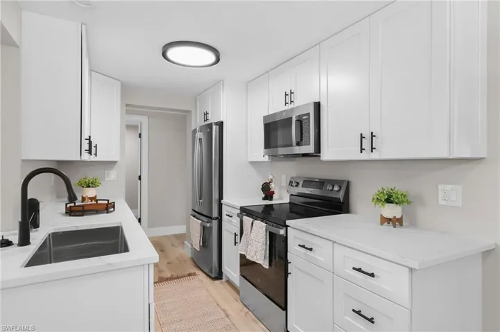 Kitchen with light stone counters, stainless steel appliances, sink, light hardwood / wood-style floors, and white cabinetry