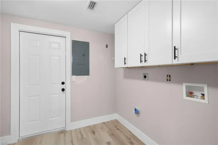 Clothes washing area featuring washer hookup, electric panel, cabinets, light wood-type flooring, and hookup for an electric dryer