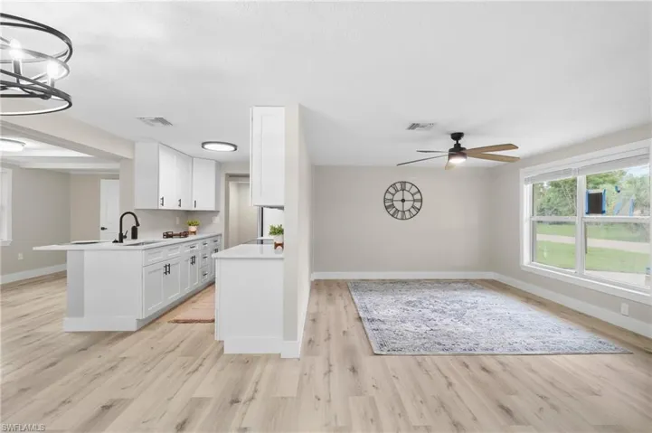 Kitchen with light hardwood / wood-style floors, ceiling fan with notable chandelier, kitchen peninsula, hanging light fixtures, and white cabinets