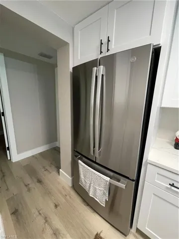 Kitchen with light hardwood / wood-style flooring, stainless steel refrigerator, light stone countertops, and white cabinetry