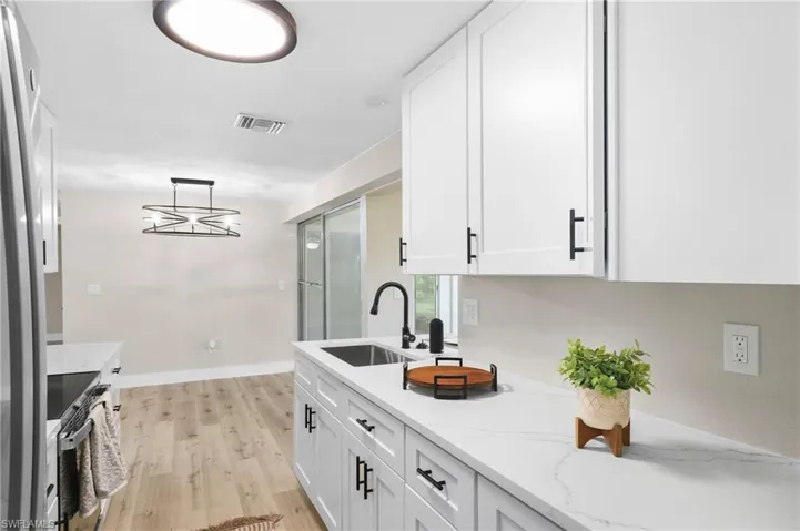 Kitchen featuring pendant lighting, white cabinets, sink, and light wood-type flooring