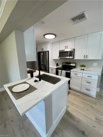 Kitchen featuring stove, light hardwood / wood-style flooring, sink, and white cabinetry