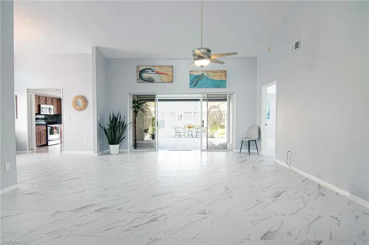 Unfurnished living room featuring light marble finish flooring, plenty of natural light, high vaulted ceiling, and a ceiling fan