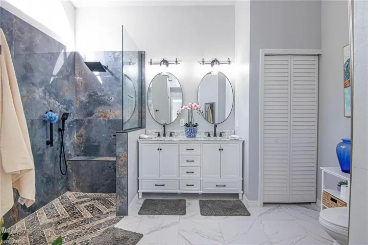 Full bathroom featuring double vanity, a marble finish shower, a closet, and light marble finish flooring