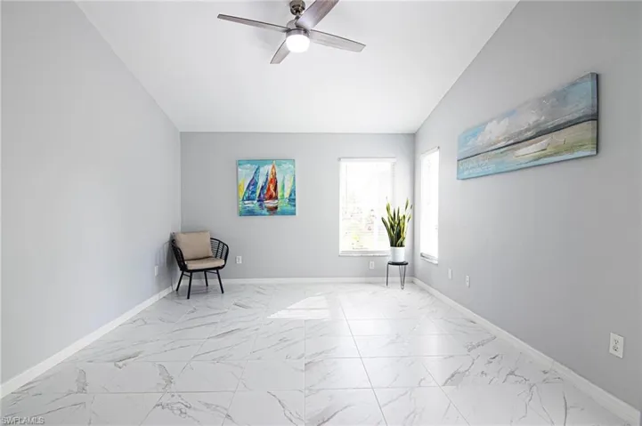 Unfurnished room featuring light marble finish flooring, lofted ceiling, and a ceiling fan