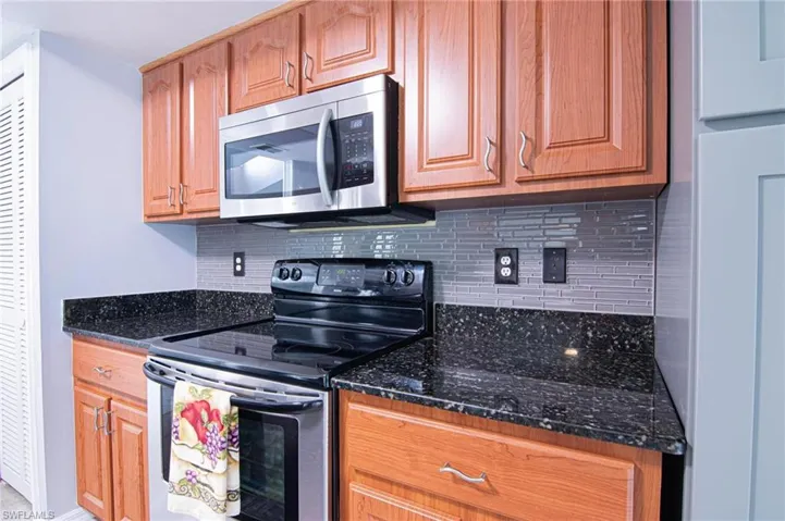 Kitchen with appliances with stainless steel finishes, dark stone counters, and brown cabinetry