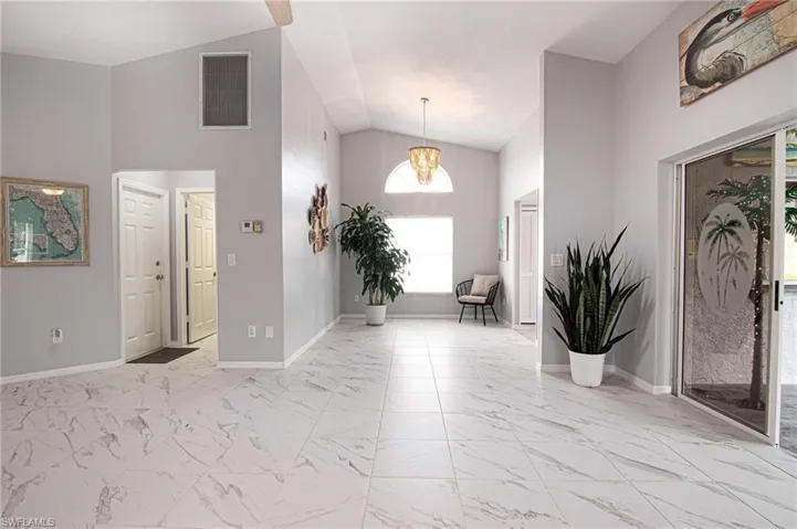 Entryway featuring light marble finish flooring, a chandelier, and high vaulted ceiling