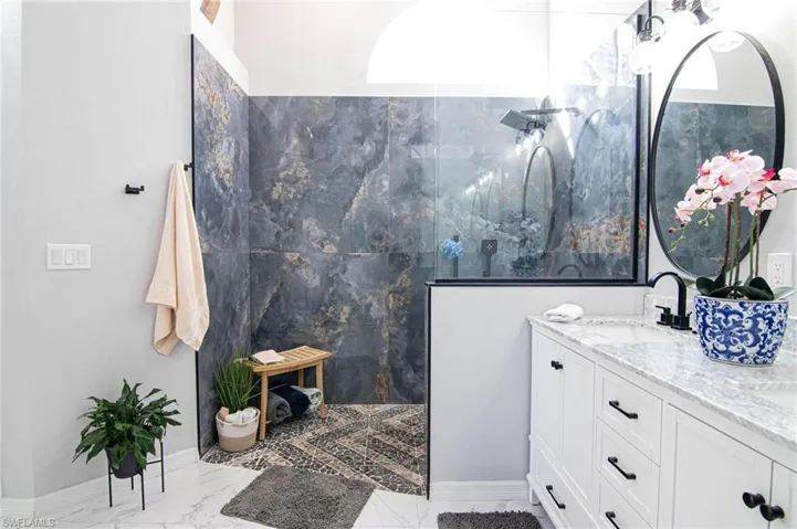 Bathroom featuring a marble finish shower, double vanity, and light marble finish flooring