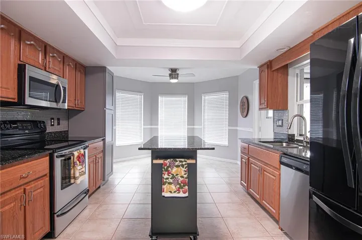 Kitchen with decorative backsplash, appliances with stainless steel finishes, brown cabinetry, and dark stone counters