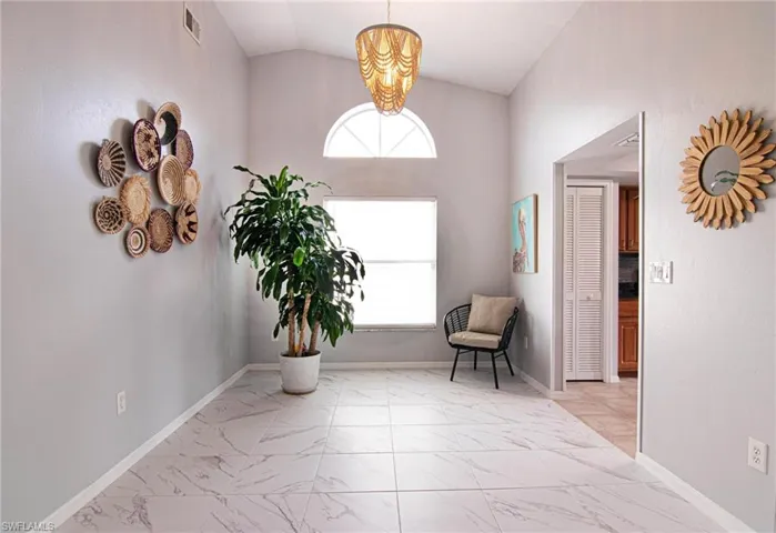 Sitting room featuring vaulted ceiling, light marble finish flooring, and a chandelier