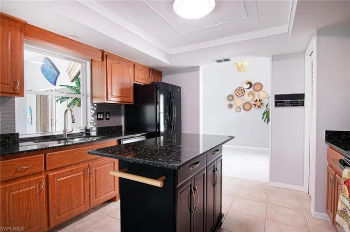 Kitchen featuring dark stone counters, a tray ceiling, a center island, and crown molding