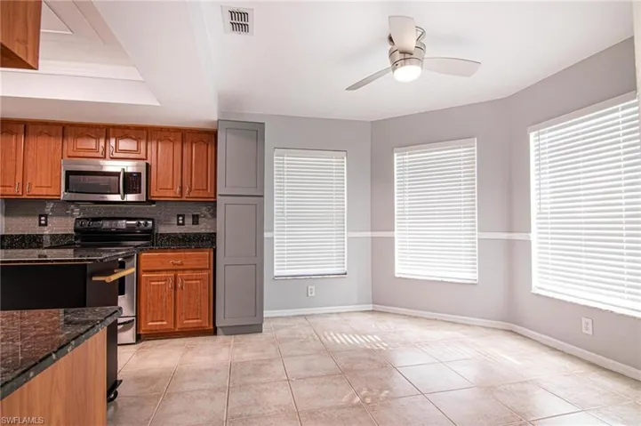 Kitchen with brown cabinetry, stainless steel appliances, backsplash, dark stone counters, and ceiling fan