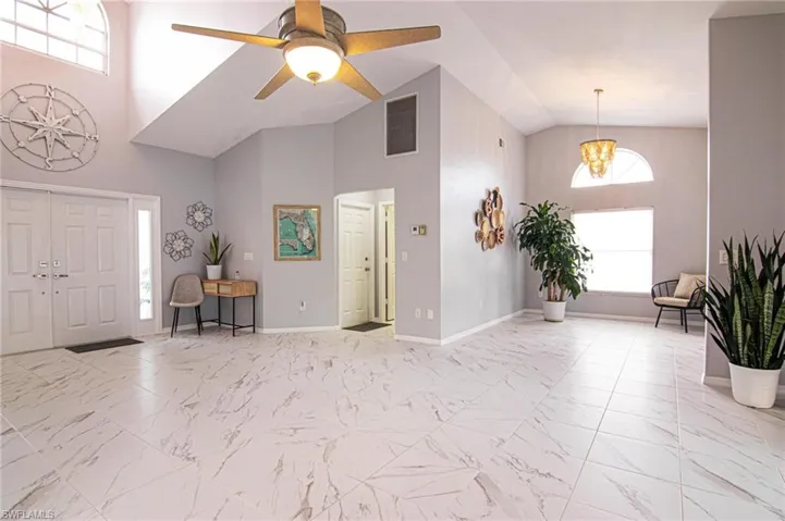 Entrance foyer with light marble finish floors, ceiling fan, high vaulted ceiling, and a chandelier