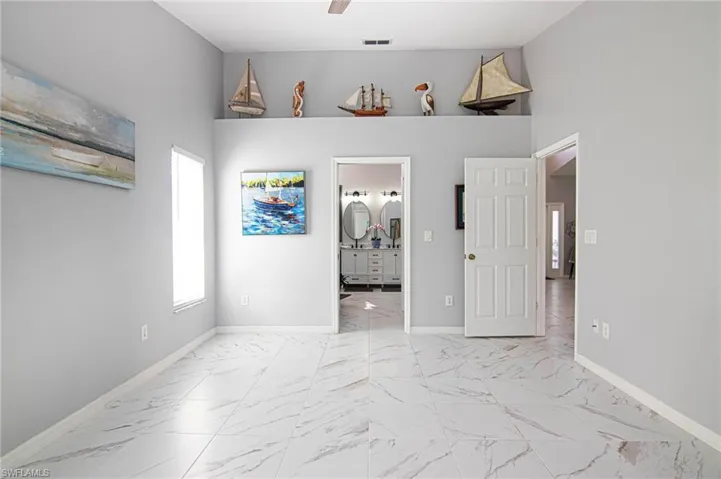 Unfurnished bedroom with light marble finish flooring, ensuite bathroom, ceiling fan, and a towering ceiling