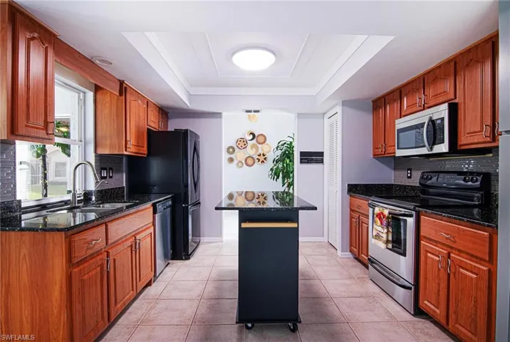 Kitchen with decorative backsplash, stainless steel appliances, dark stone countertops, and brown cabinetry