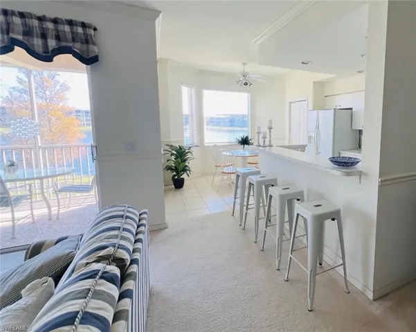 Kitchen with a breakfast bar, ornamental molding, light carpet, a ceiling fan, and white fridge with ice dispenser