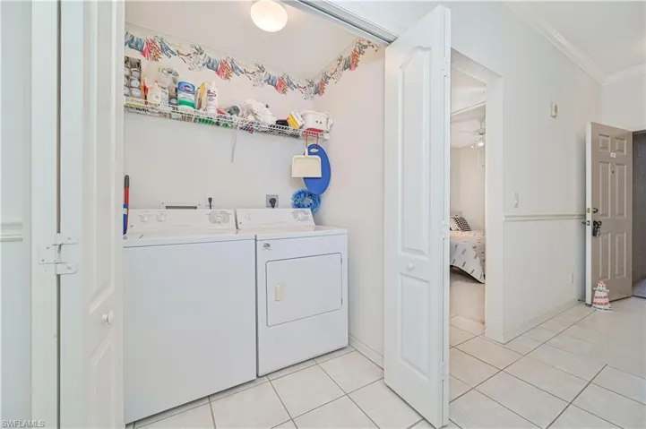 Laundry room featuring light tile patterned floors, ornamental molding, washer and dryer, and a ceiling fan