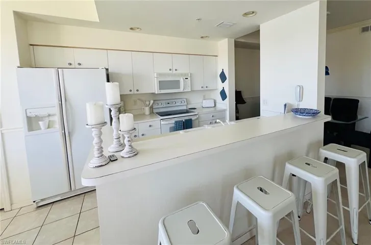 Kitchen with white appliances, light countertops, a kitchen bar, light tile patterned floors, and white cabinetry