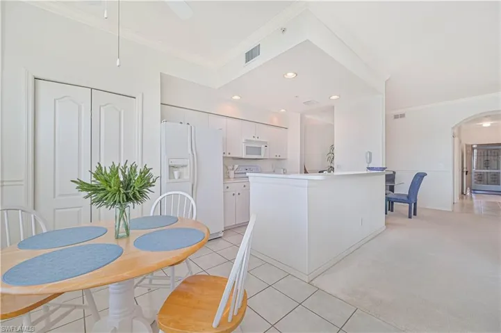 Kitchen with crown molding, white cabinets, white appliances, light carpet, and arched walkways