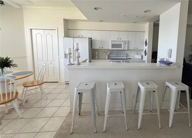 Kitchen with a kitchen bar, light countertops, a peninsula, white appliances, and light tile patterned flooring