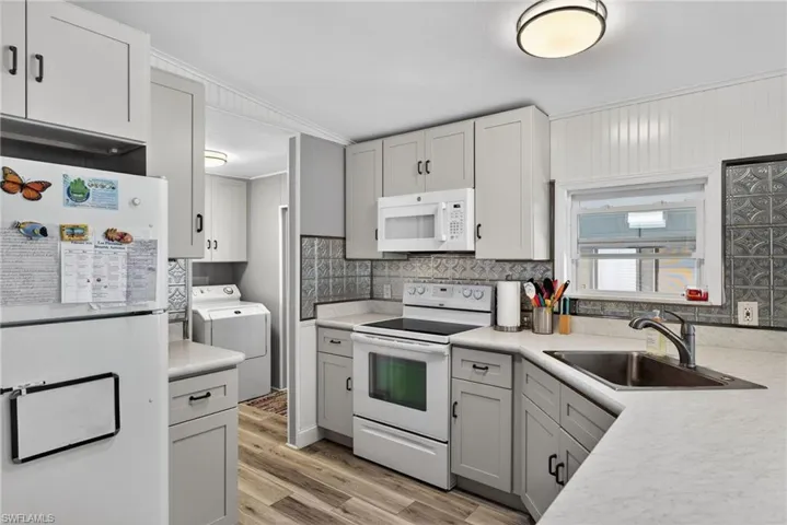 Kitchen featuring white appliances, light countertops, light wood-type flooring, washer / dryer, and white cabinetry