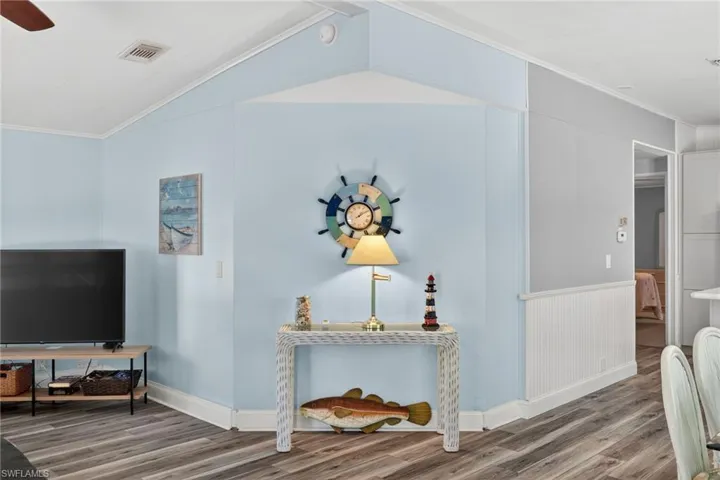 Living room with ornamental molding, light wood-style flooring, a ceiling fan, vaulted ceiling, and wainscoting
