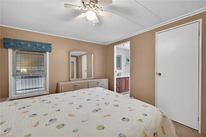 Bedroom with ornamental molding, ensuite bath, ceiling fan, and carpet